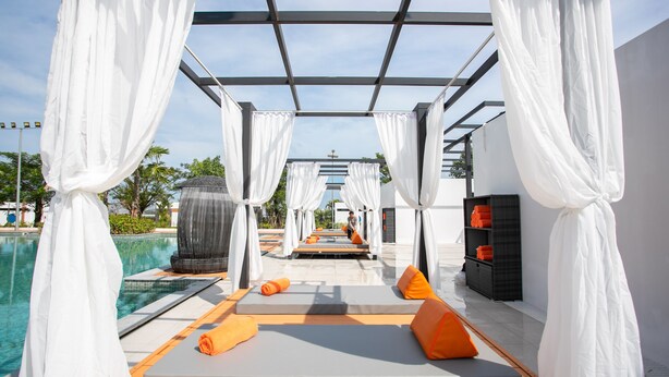 A poolside area with white canopies, orange cushions, and a clear view of the pool.
