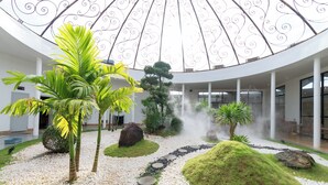 A modern building with a circular atrium, a central garden with palm trees, and a decorative metal ceiling.