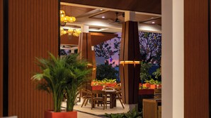 An indoor dining area with wooden furniture, potted plants, and pendant lighting.