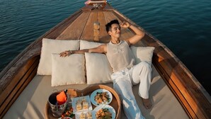 A person relaxing on a boat with a tray of food and drinks.