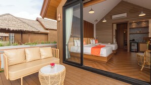 A modern hotel room with a large sliding glass door, a sofa, a round table, and a bed with a wooden headboard.