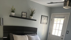 A bedroom with a large bed, a dark headboard, a ceiling fan, a window, and a door. - Cozy little place 
15 min from the strip  (Las Vegas)