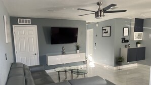 A modern living room with a grey sofa, a flat-screen TV, a ceiling fan, and a minimalist design. - Cozy little place 
15 min from the strip  (Las Vegas)