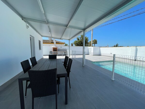 A covered patio with a pool, outdoor seating, and a grill area.