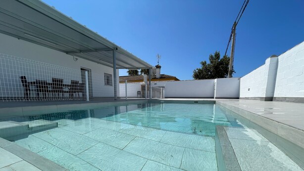 Piscina com água cristalina, rodeada por um muro branco e uma área coberta com telhado.