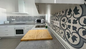 Uma cozinha moderna com armários brancos, micro-ondas, torradeira e tábua de corte de madeira.