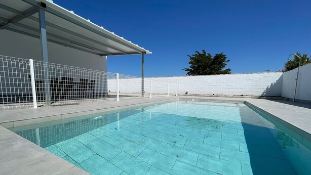 A rectangular swimming pool with a tiled deck, a white fence, and a clear blue sky. - Miamar II House in Chiclana (Chiclana)