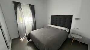 A modern bedroom with a large bed, a small round table, and a window with sheer curtains. - Miamar II House in Chiclana (Chiclana)