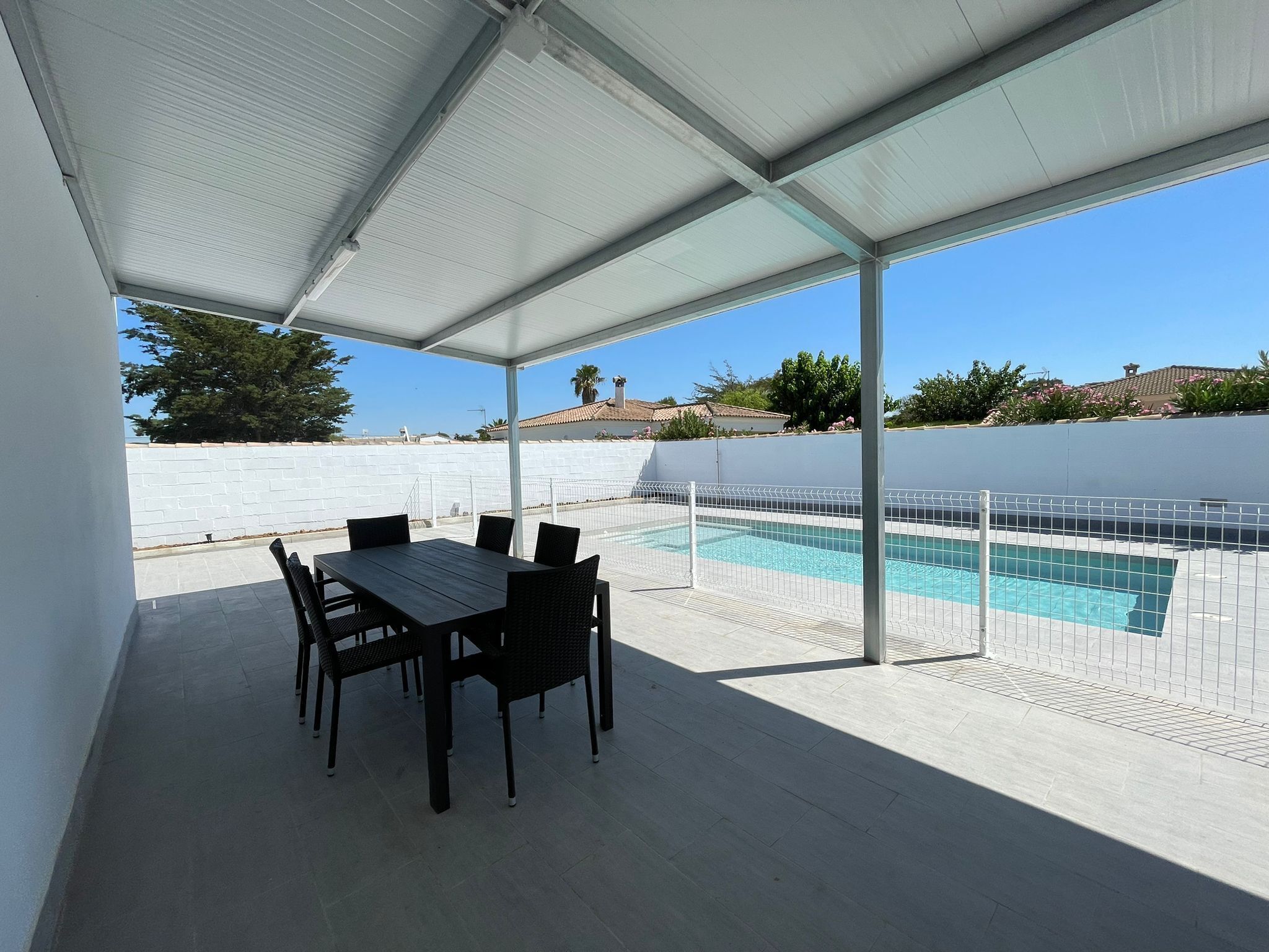 Un patio couvert avec une piscine, du mobilier d’extérieur et une vue sur les environs.
