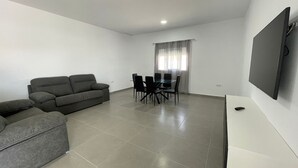 A living room with a sofa, dining table, chairs, and a TV. - Miamar II House in Chiclana (Chiclana)