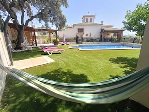 A backyard with a swimming pool, a hammock, and a house with a tiled roof.