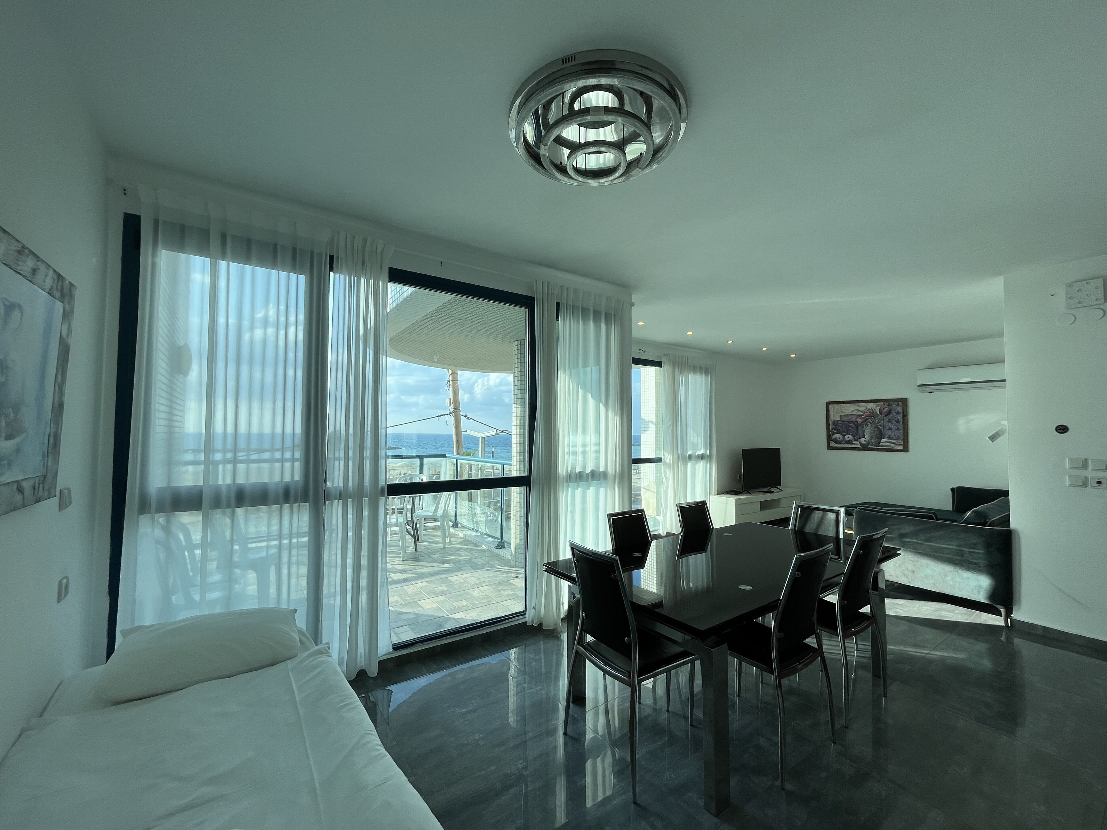 A modern hotel room with a large balcony, a dining area, and a TV.