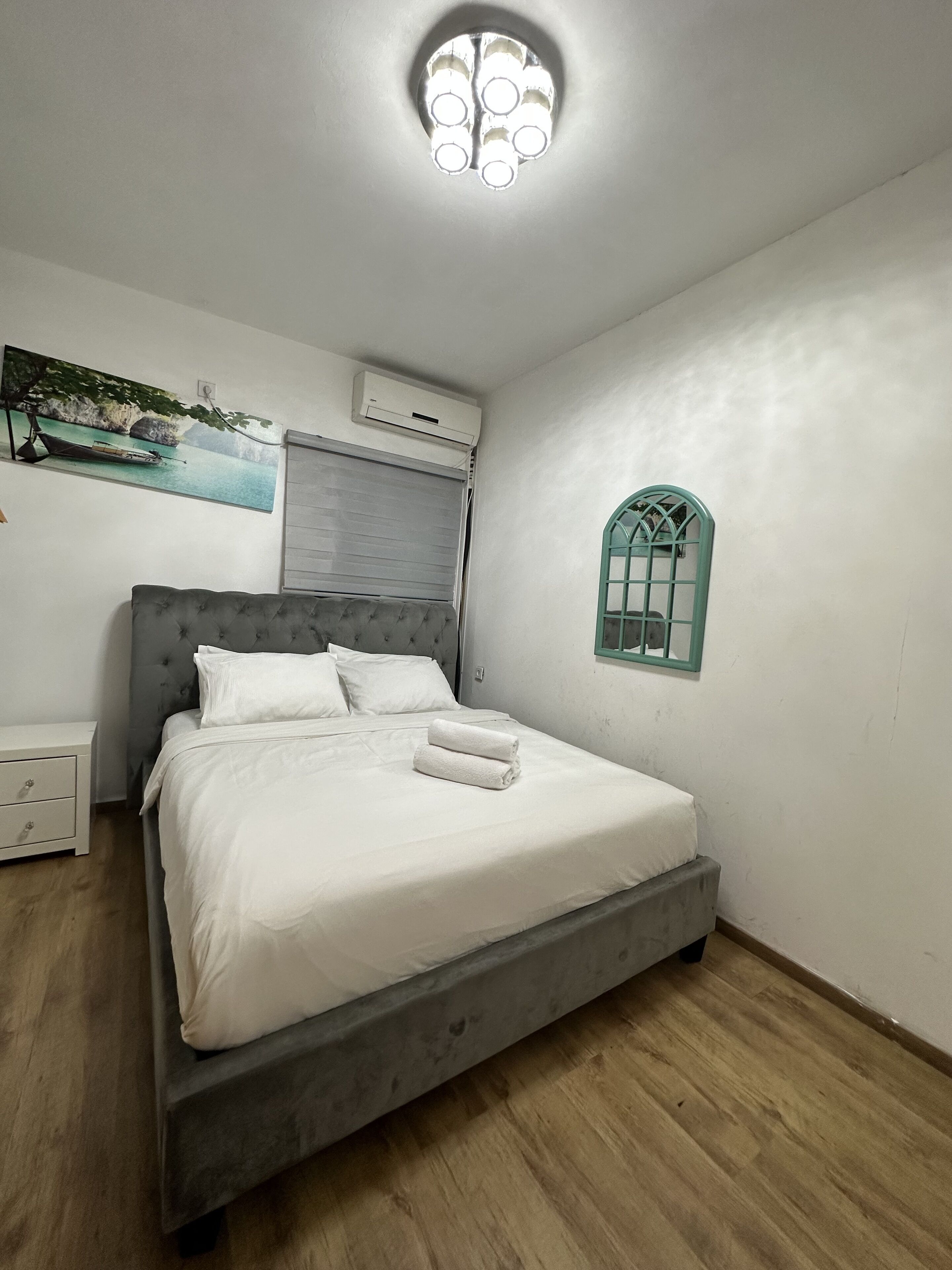 Ein Schlafzimmer mit einem Bett, einem Nachttisch, einer Klimaanlage, einem Fenster und einem Bild von einem Boot.
