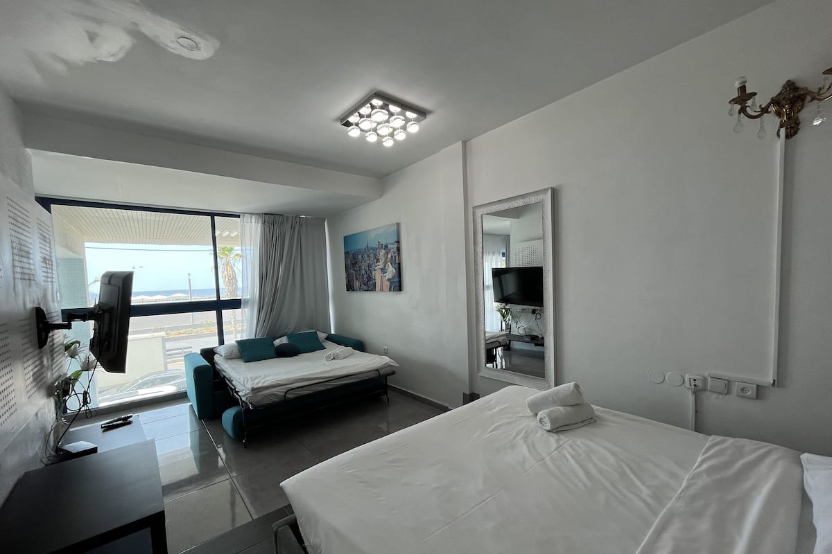 Une chambre d’hôtel moderne équipée d’un lit, d’un bureau avec un ordinateur, d’une télévision et d’une grande fenêtre donnant sur l’extérieur.