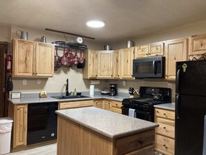 A kitchen with wooden cabinets, a granite countertop, a black stove, a microwave, and a refrigerator.