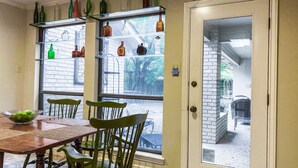 A dining area with a wooden table and green chairs, a window with decorative bottles, and a door leading to an outdoor area. - Centrally located, elegant, spacious, home, large screen tv, pool & ping pong! (Huntsville)