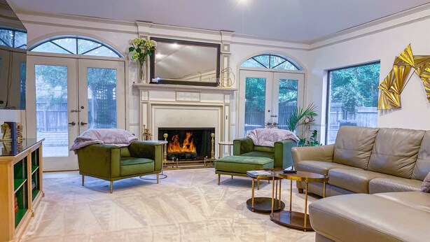A spacious living room with a fireplace, green armchairs, a beige sofa, and large windows. - Centrally located, elegant, spacious, home, large screen tv, pool & ping pong! (Huntsville)