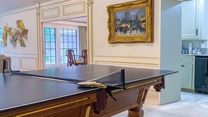 A ping pong table in a room with a painting and a window. - Centrally located, elegant, spacious, home, large screen tv, pool & ping pong! (Huntsville)
