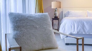 A hotel room with a bed, a chair with a fluffy pillow, a bedside table with a lamp, and curtains. - Centrally located, elegant, spacious, home, large screen tv, pool & ping pong! (Huntsville)