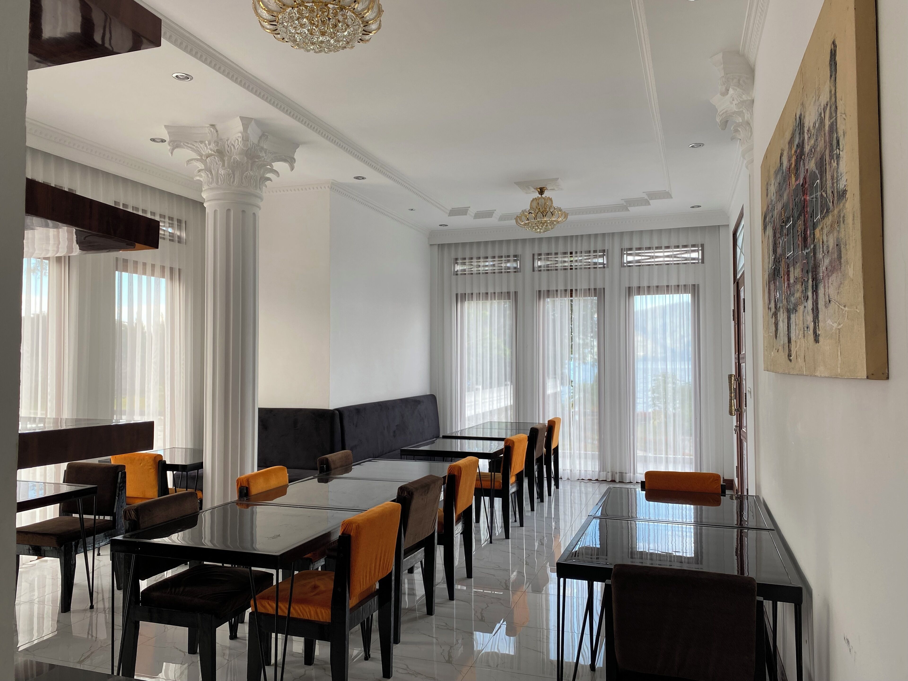 Un espace de restauration moderne avec des tables et des chaises en verre, des colonnes blanches et un grand tableau mural.