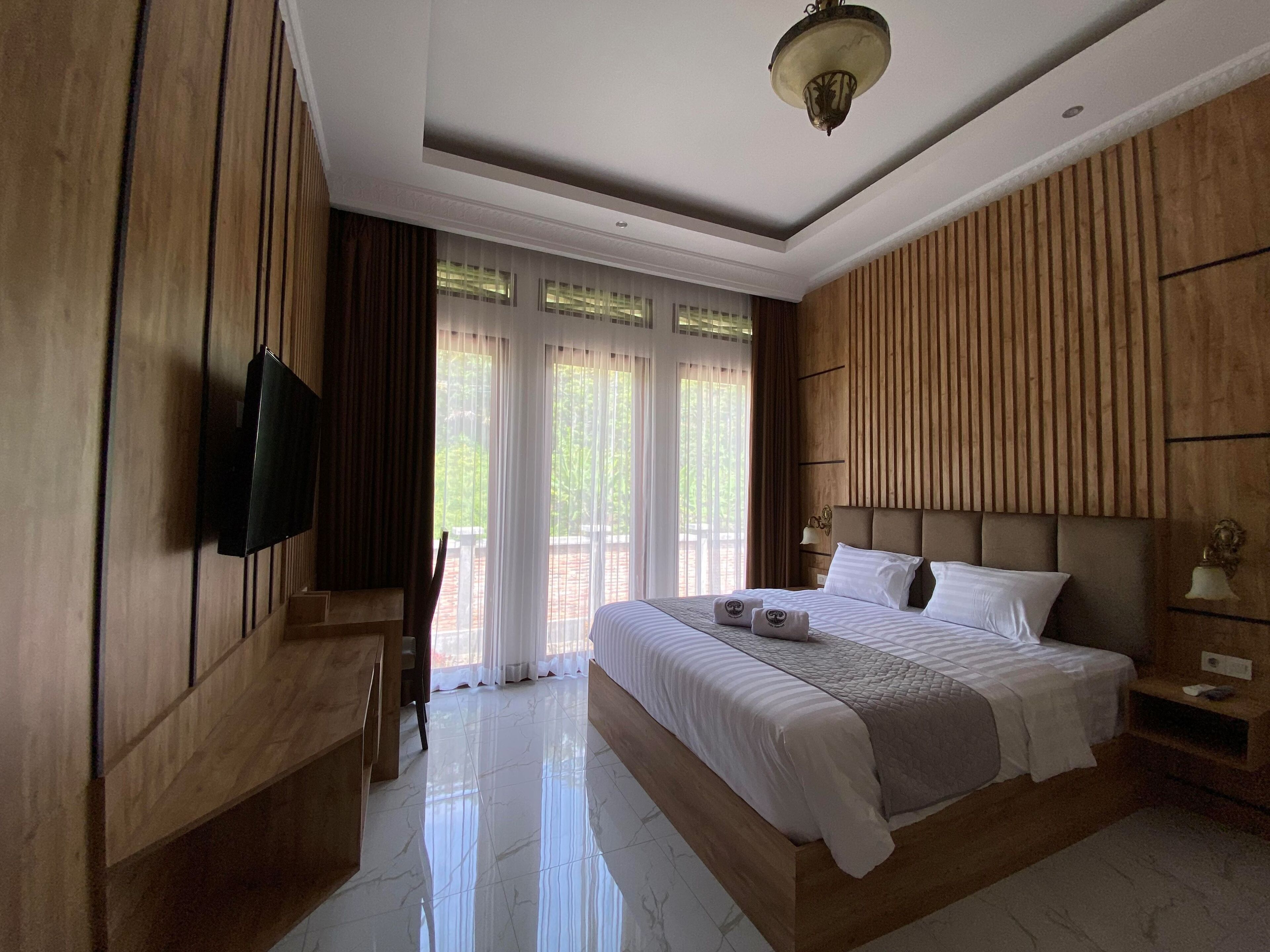 A hotel room with a large bed, wooden paneling, a flat-screen TV, and a balcony with curtains.
