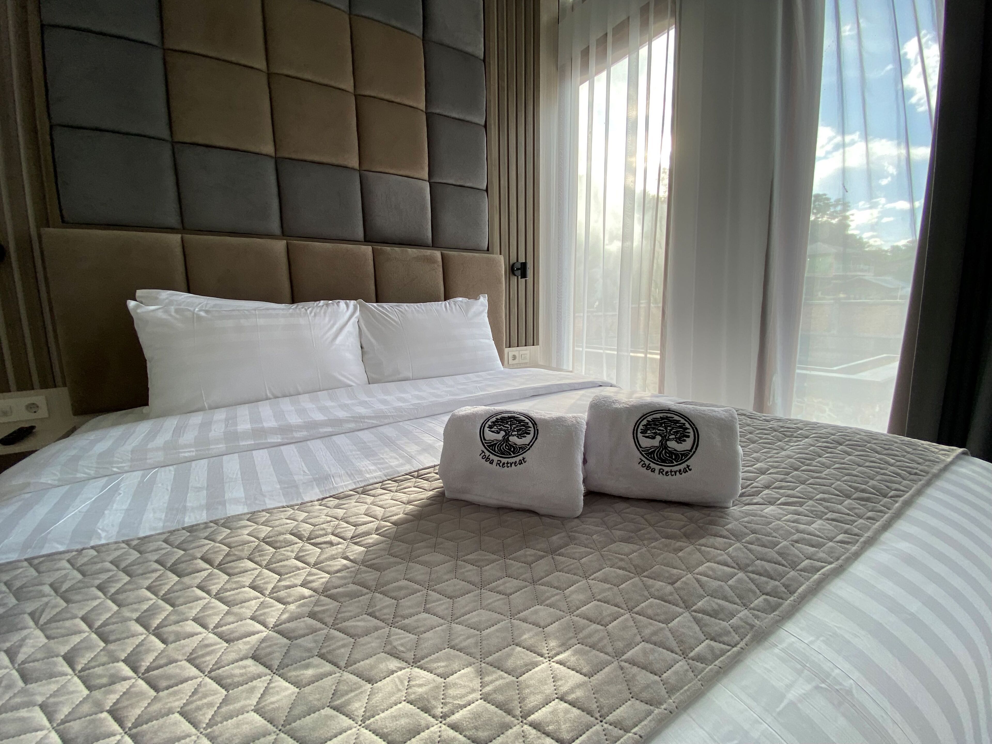 A hotel room with a large bed, a headboard, and two towels with a logo.