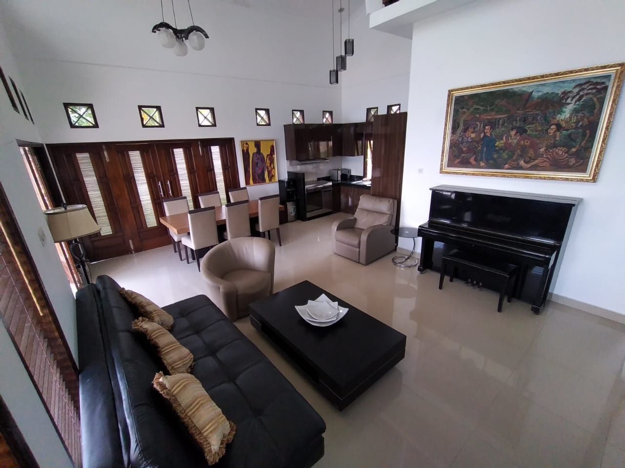 Amplia sala de estar con un sofá negro, una mesa de centro y un piano. Hay varias sillas y un comedor con una mesa y sillas.