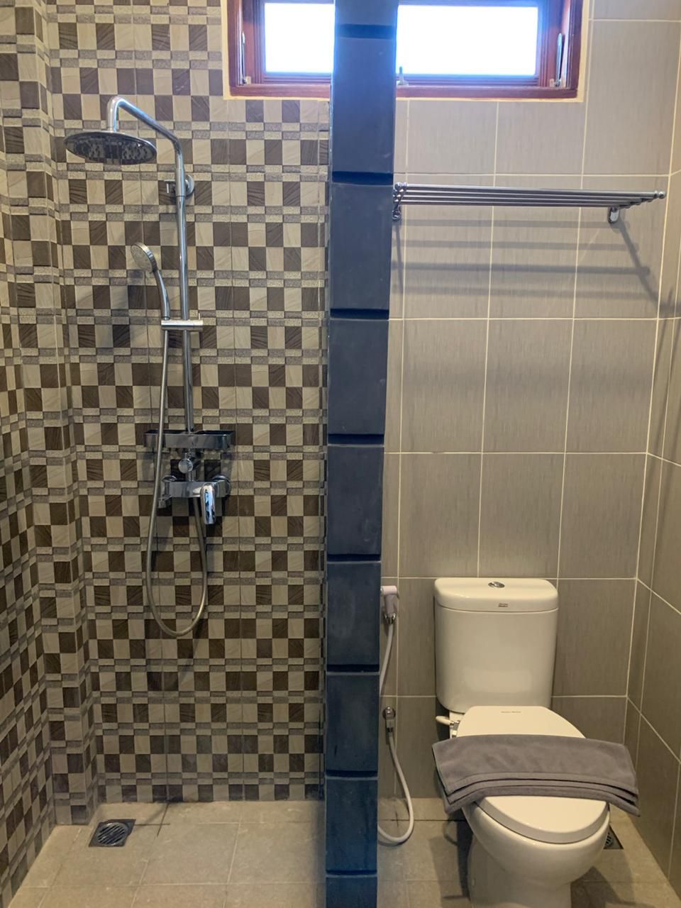 A bathroom with a checkered tile wall, a shower, a toilet, and a towel rack.