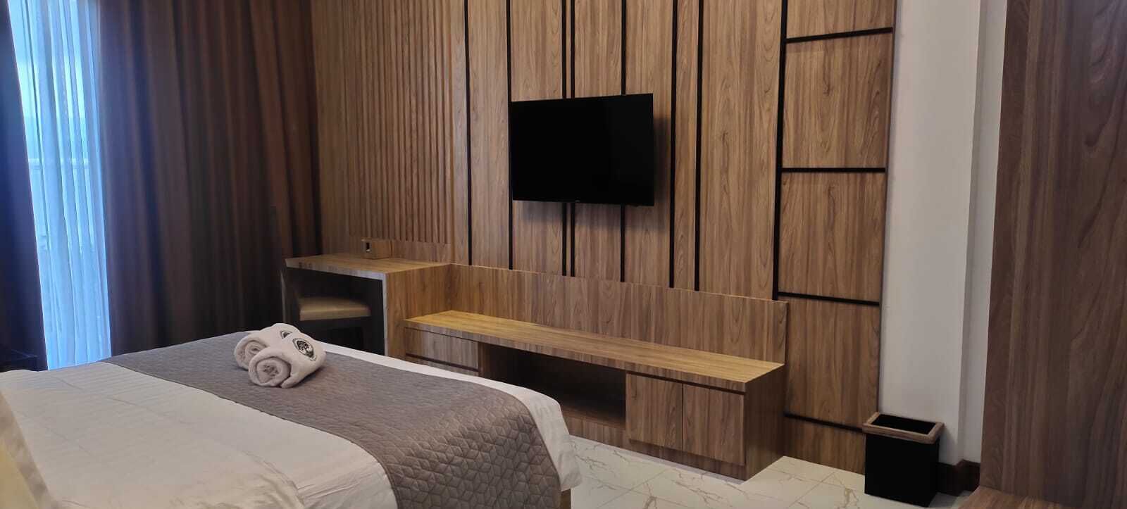 Une chambre d’hôtel moderne, équipée d’un lit, d’un téléviseur fixé au mur sur un panneau en bois, d’un petit banc en bois et d’une table de chevet.