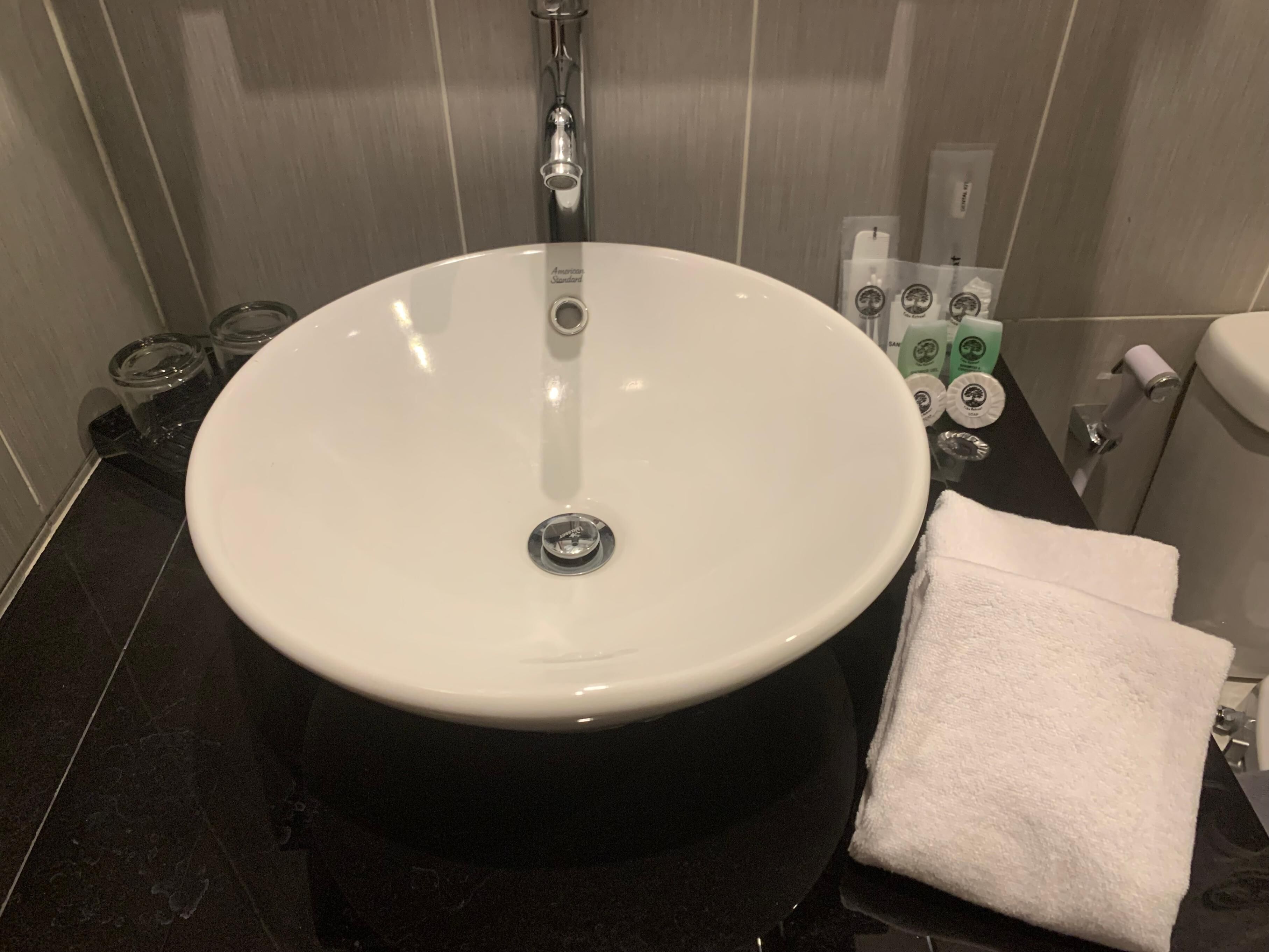 A bathroom with a round white sink, a towel, and toiletries on the counter.