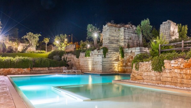 A swimming pool with stone walls and greenery, surrounded by a well-lit patio area. - Cava Li Santi Residence - Villa La Cava | Appartamento Deluxe (Santa Caterina)