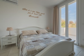 Une chambre à coucher avec un lit, deux tables de chevet, un mur orné d’une citation et une vue accessible par une porte coulissante.