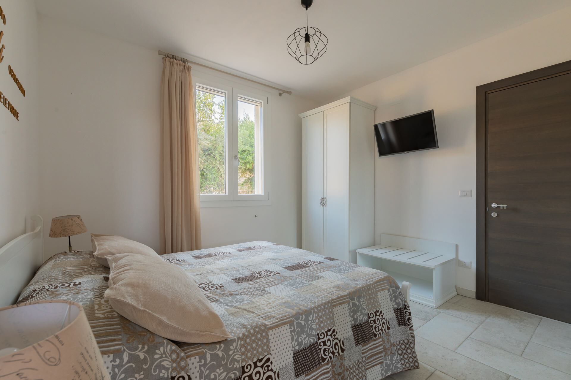 A bedroom with a bed, a bedside table, a lamp, a wardrobe, a TV mounted on the wall, and a door.