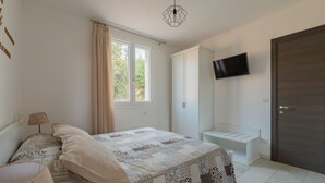 A bedroom with a bed, a bedside table, a lamp, a wardrobe, a TV mounted on the wall, and a door. - Cava Li Santi Residence - Villa La Cava | Appartamento Superior (Santa Caterina)