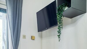 Ett rum med en gul stol, ett litet svart bord, en tv som är monterad på väggen och en växt som hänger bredvid tv:n.