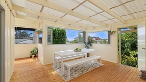 A sunlit room with a wooden floor, a white bench, and a table with potted plants.