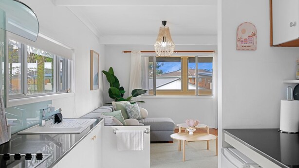 A modern kitchen with a built-in oven, a dining area with a small table and chairs, and a seating area with a sofa and a large plant.