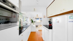 A modern kitchen with white cabinetry, a Miele refrigerator, and a coffee machine.