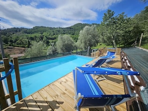 Un terrazza in legno con piscina, sedie a sdraio e vista su un pendio boschivo.