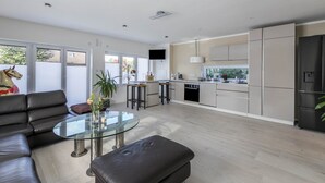 Een moderne keuken met een centraal eiland, een eethoek met een glazen tafel, en een woonkamer met een leren bank.