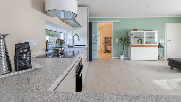 Een moderne keuken met granieten werkbladen, een roestvrijstalen afzuigkap en uitzicht op de woonkamer.