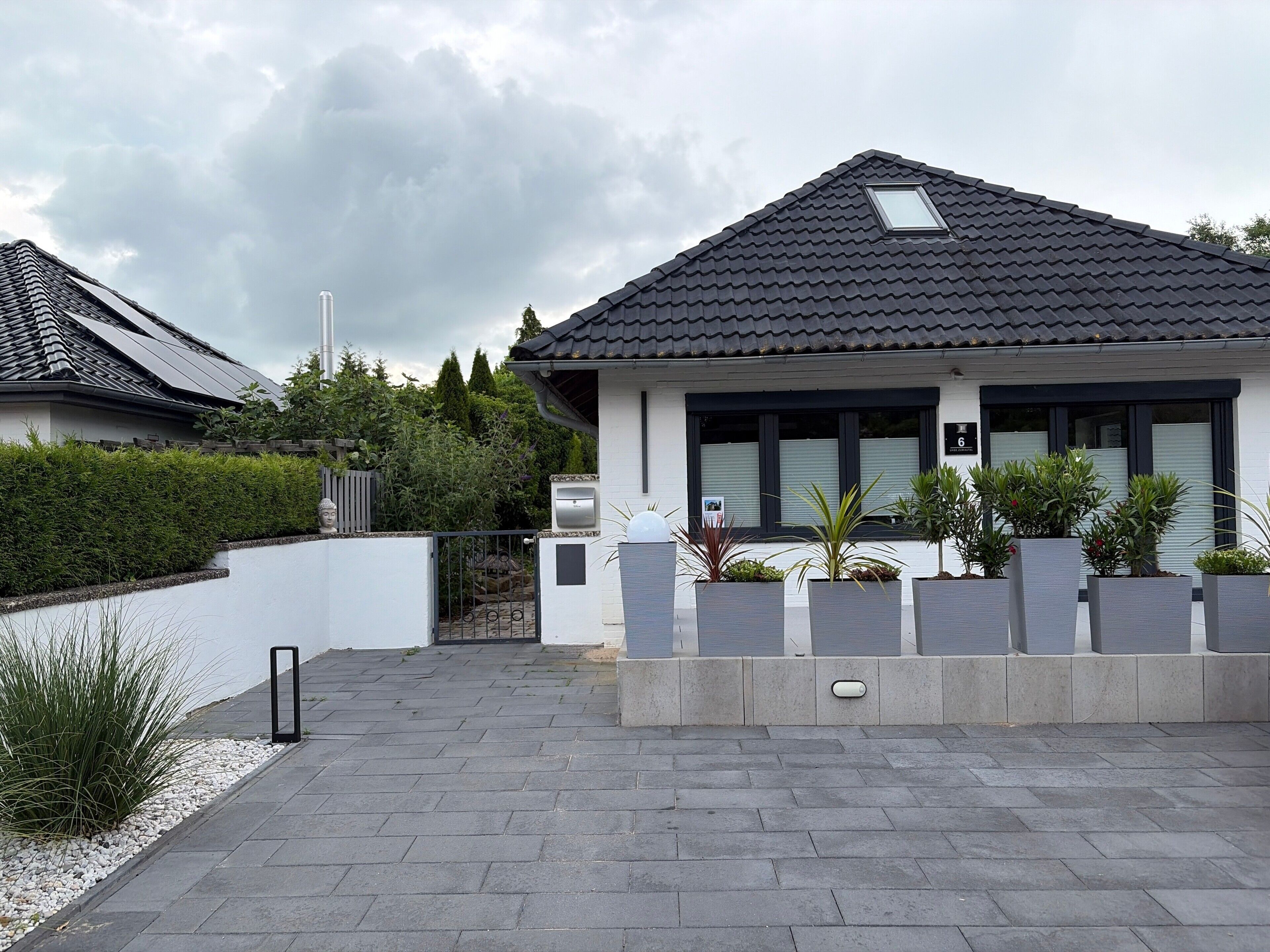 A modern house with a tiled roof, a gated entrance, and potted plants.