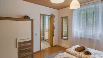 Een slaapkamer met een kledingkast, een spiegel, een bed met handdoeken en een raam met dunne gordijnen.