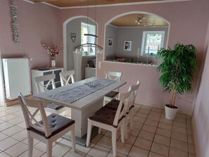 A dining area with a white table, four chairs, a hanging light fixture, and a potted plant.