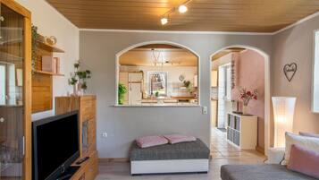 A modern bedroom with a TV, a bed, and a view of the kitchen through an archway.