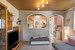 A modern bedroom with a TV, a bed, and a view of the kitchen through an archway. - Holiday Apartment "Fewo 2 - Osterberg" with Private Terrace, Shared Garden & Wi-Fi (Liebenau)