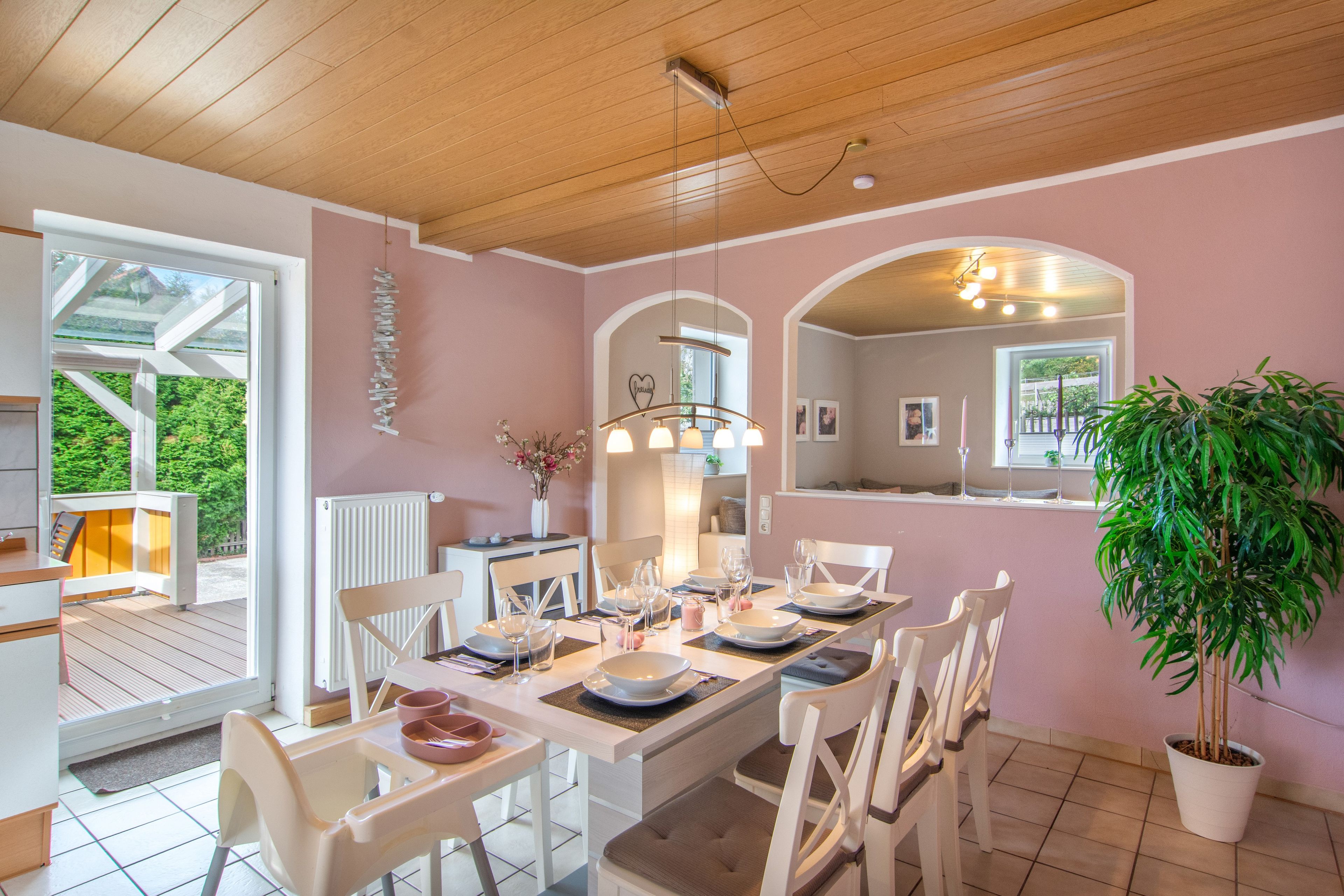Un comedor con una mesa dispuesta para cuatro, sillas blancas y una planta en maceta.