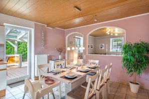 Un coin repas avec une table dressée pour quatre personnes, des chaises blanches et une plante en pot.