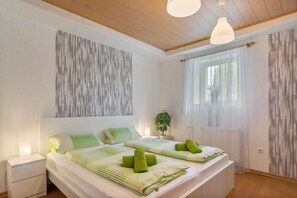 Une chambre à coucher moderne avec un grand lit, une table de chevet, une plante en pot et une fenêtre ornée de rideaux légers.