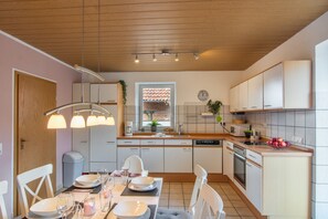 A modern kitchen with wooden cabinets, a dining area with a table set for two, and a window with a view of the outside. - Holiday Apartment "Fewo 2 - Osterberg" with Private Terrace, Shared Garden & Wi-Fi (Liebenau)